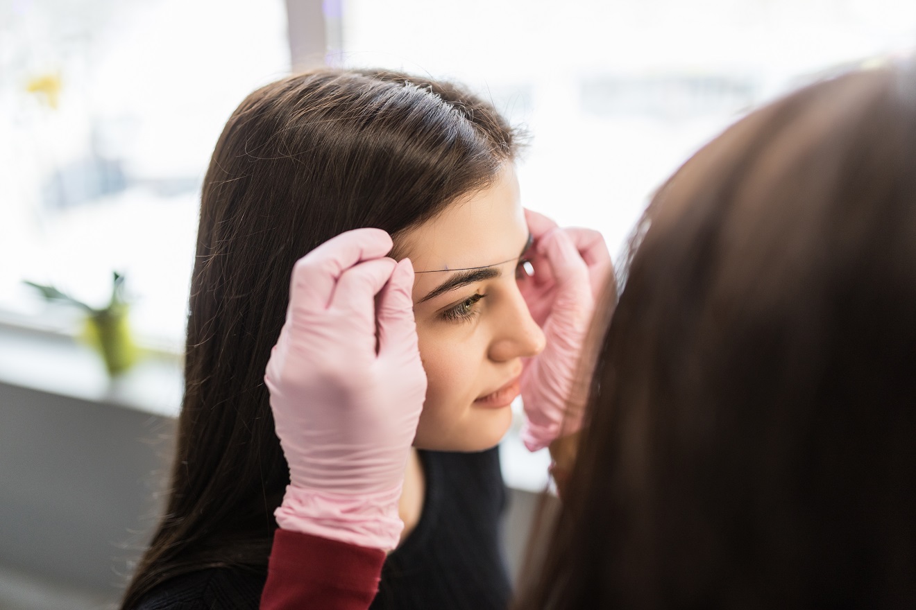 pretty female master in white gloves determine eyebrow contour on young model